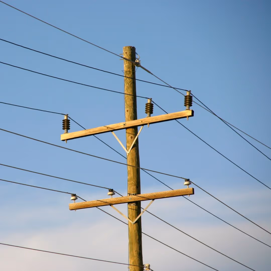 Wooden utility pole with multiple power lines against a clear blue sky